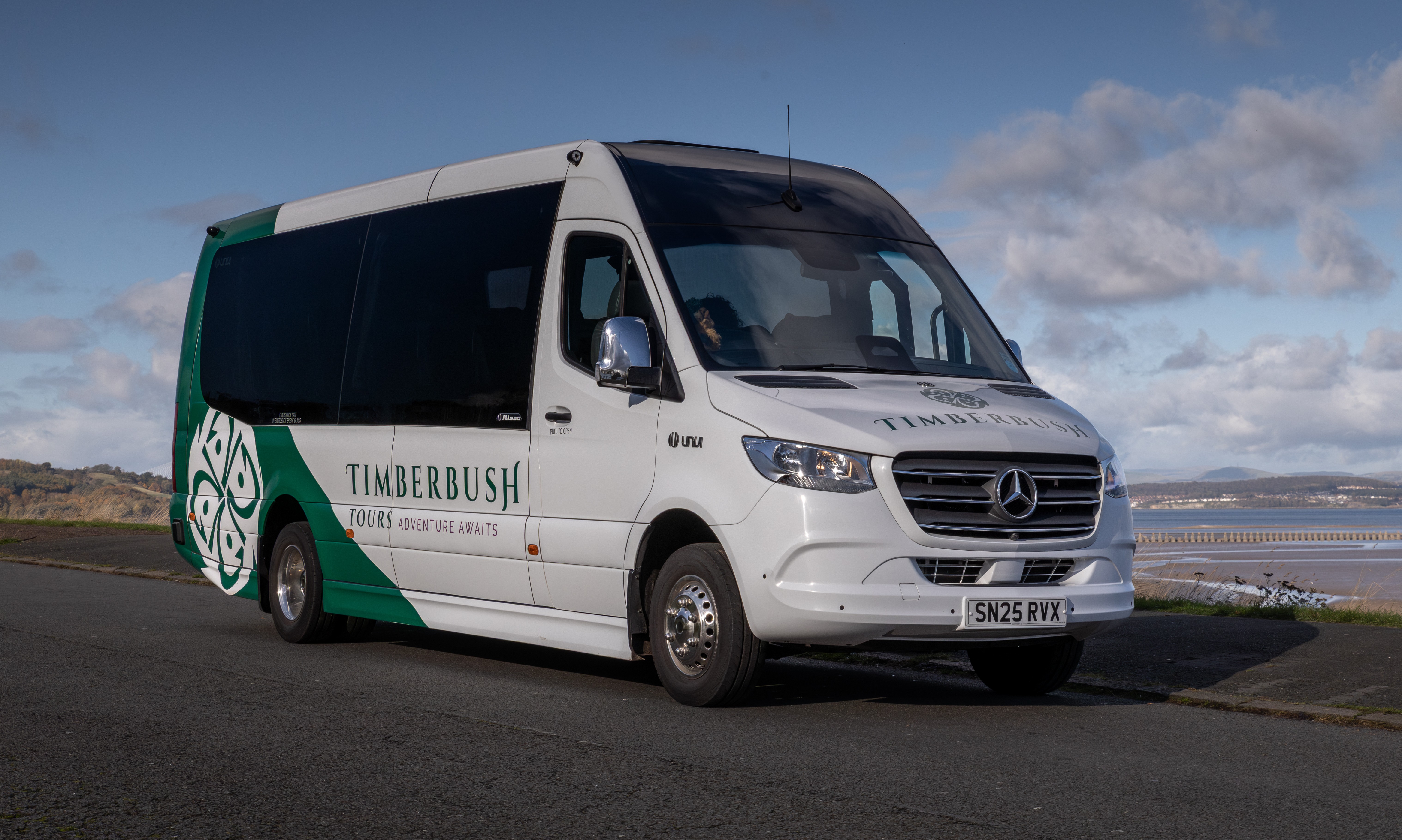 A smaller tour coach with a beach in the background